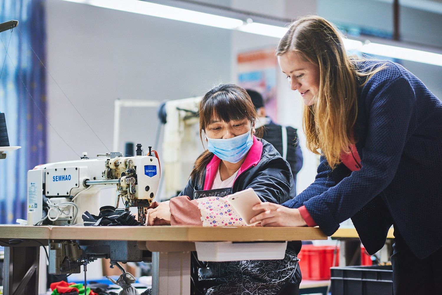 Marianne Hughes speaking with a garment worker beside an industrial sewing machine